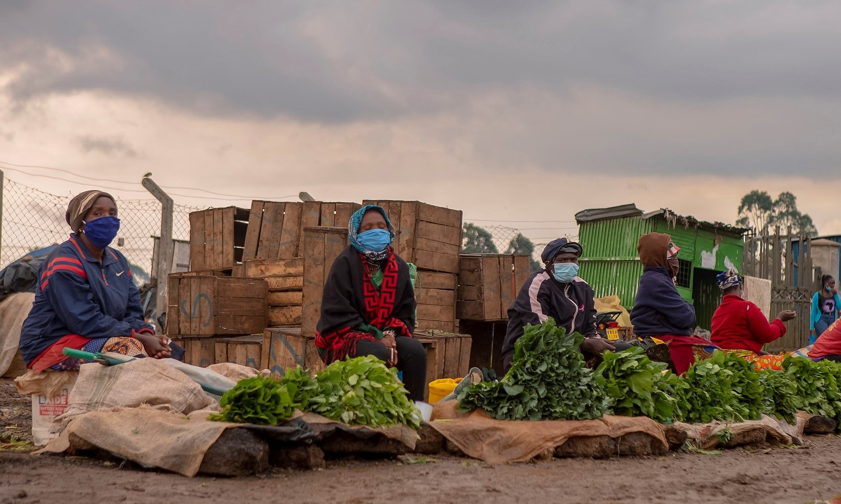 Women with masks keep their distance at the market where they sell their vegetables. 