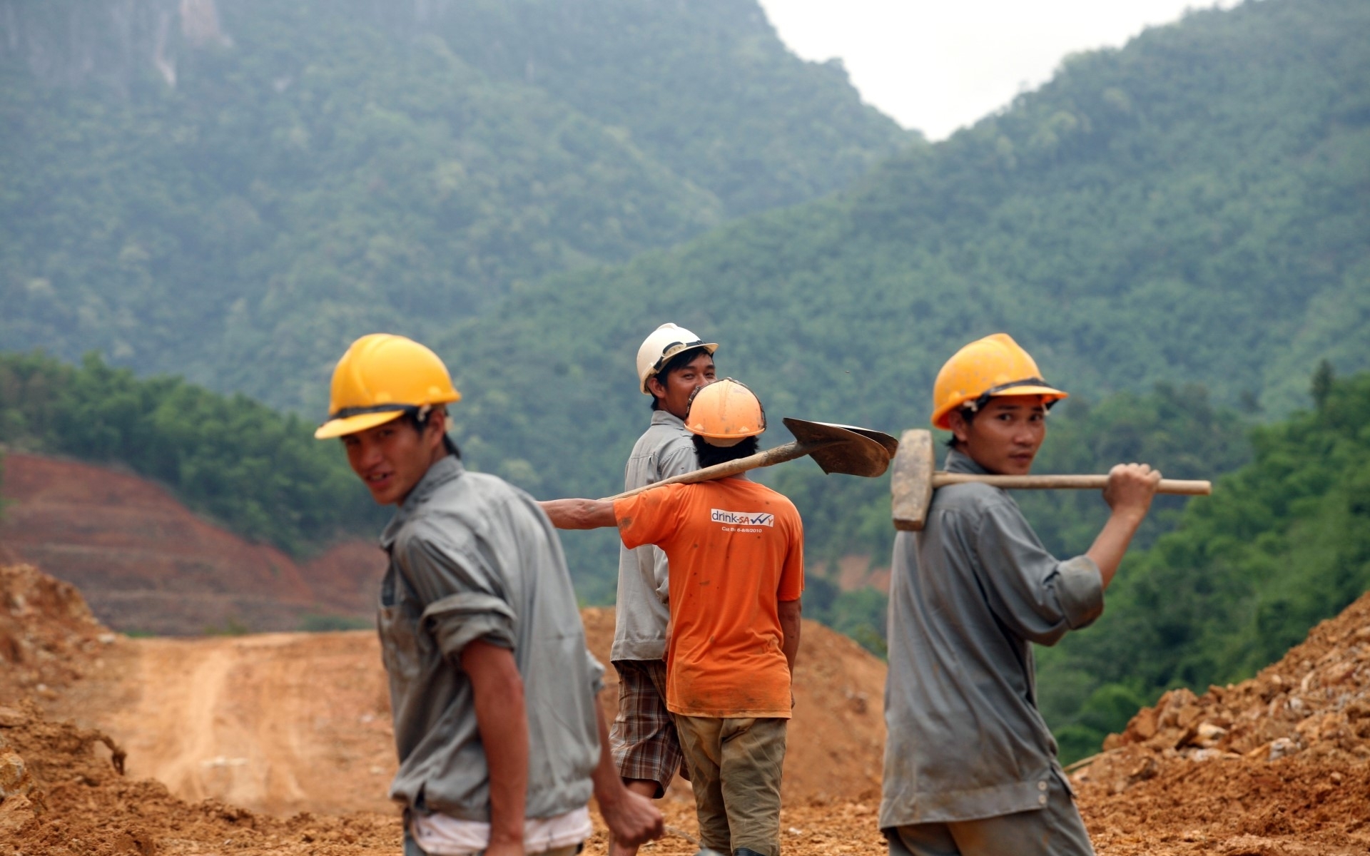 Four men in working clothes and with tools on a mound of earth. 