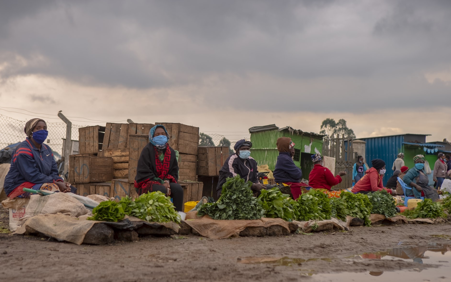 Des femmes portant des masques respectent la distanciation sur le marché où elles vendent leurs légumes. 